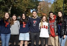 A group of students wearing Penn-branded clothing stand outsdie with their arms around each other.