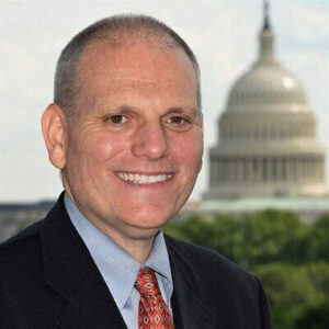 A man in a suit smiles in front of the Capital Building
