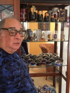 Robert Weisman stands in front of his bookcase with Murano glass and Israeli prime minister nesting dolls. Photo by Jon Marks 