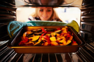 a woman looks at roasted vegetables in the oven
