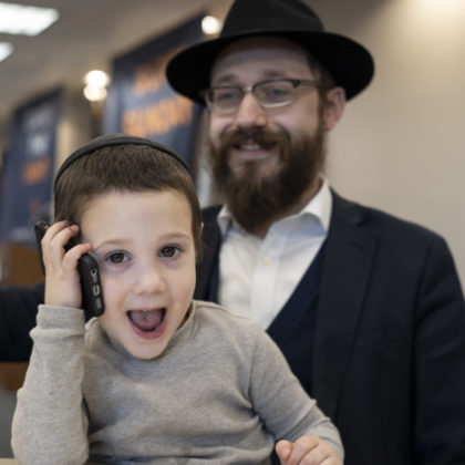 Rabbi Hirshi Sputz looks on as his son, Zalmi, works the phones at Super Sunday in Center City.