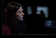 The photos is a profile of Maia Levy, who is an Israeli women in her early 20s with long, brown, curly hair. She is in a dark room looking at a screen.