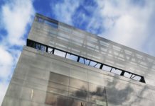 The tall, glass exterior of the NMAJH reaches up five stories. In front of the building is a marble statue of a women standing in front of a nude boy and an eagle.