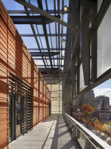 A corridor of the NMAJh has bronze walls on one side and a balcony overlooking autumn trees and historic Philadelphia buildings on the other.