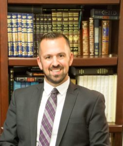 Rabbi Nathan Weiner is a white man with brown eyes, short brown hair, and a cropped beard wearing a suit and smiling in front of a bookshelf.