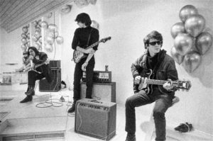 Dressed in all black and sunglasses, members of the Velvet Underground are reclined with their instruments.