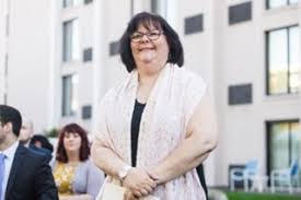 Mimi Ferraro is a while woman with shoulder-length dark hair and bangs wearing glasses and a tallit. She is smiling and standing outside.
