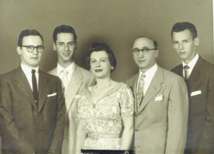 In a sepia image, Jacques Lipetz, a young man with short hair and no beard is wearing a suit and horn-rimmed glasses. He is to the right of his two brothers and mother and father.