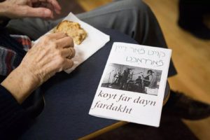 On someone's lap is a piece of cake someone is picking at, as well as a program printed on white paper that reads "koyt far dayn fardakht," the name of a Yiddish anarchist punk band.