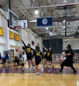 During a basketball game, one member of the opposite team goes in for a layup, while a Kohelet player flies in the air with her hands up, blocking the shot.