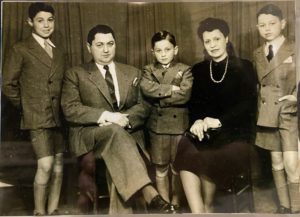 In a sepia photo, Claude Boni is standing between his parents with his arms crossed. His brother flank his parents on either side of the photo.