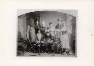 A black-and-white photo shows a handful of adults wearing various costumes posing in two rows.