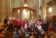 In the sanctuary of a synagogue, dozens of children and adults dressed up pose sloppily for a group picture.