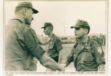 In a black-and-white photo, a young white soldier is shaking hands with an older white soldier, both in uniform.