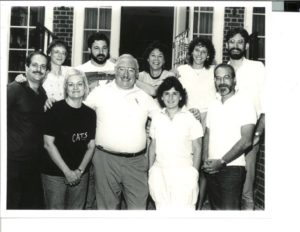 In a black and white photo, two rows of people smile at the camera.