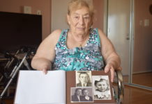 Bronislava Kerzhnerman is an older white woman wearing a sea floam green top. She is holding a photo album of her and her parents when they were younger.