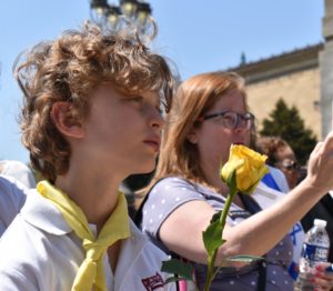 A young boy holds a yellow rose and looks thoughtful.