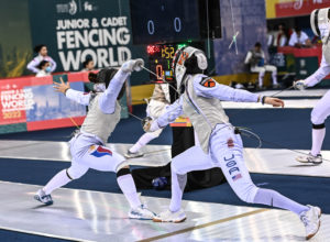 Two fencers in full uniforms are lunging, their foils extended.