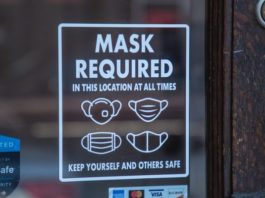 A decal on a glass window reads "MASK REQUIRED". Below the words are pictures of various types of masks.