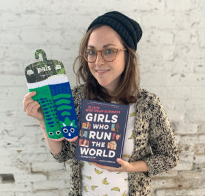 Hannah Lavon holding up a book she wrote and a pair of socks.