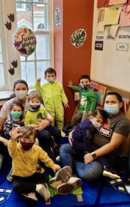 In a classroom, a group of kids wearing masks and kippot and looking at the camera and smiling.