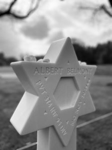 A black and white picture shows a Star of David gravestone with stones placed on top of it.