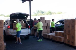 Volunteers in bright yellow shirts load cardboard boxes into a hatchback car.