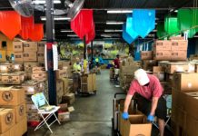 In a warehouse, volunteers pack boxes in a socially distanced manner.