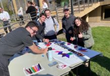 At a table outside, five Hillel members color a banner with markers.