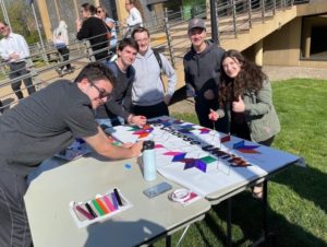 At a table outside, five Hillel members color a banner with markers.