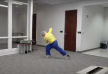 Jonathan Stein, a white man wearing a yellow shirt and blue pants, dances in the middle of his law office.