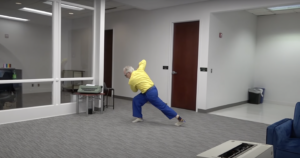 Jonathan Stein, a white man wearing a yellow shirt and blue pants, dances in the middle of his law office.