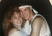 A young couple dressed in typical '80s clothing are hugging and smiling at the camera.