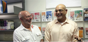 Two bald white men wearing collared shirts stand next to each other and laugh.