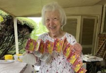 Marcia Bass Brody is a white woman standing outside holding a long string of lottery tickets and smiling.