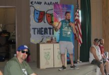 Rabbi Nathan Weiner is a white man in a t-shirt and shorts standing on a stage at summer camp.