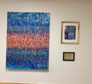 A blue and coral abstract painting hangs on a white wall.