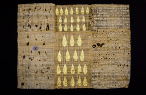 A piece of papyrus with circular scorch marks has a row of gold drops running through it.