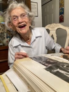 Elizabeth Bleiman is a white woman with short, grey hair and glasses smiling with a photo album in front of her.