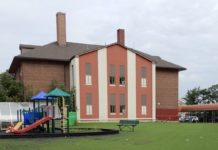 A brick building with a playground and grass field on an overcast day