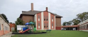 A brick building with a playground and lawn on a cloudy day