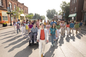 Evan walks down the street on his Indiana town, the students at his school behind him in a triangle formation.
