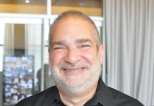 Rabbi Jacob Staub is a white man with buzzed hair and a short, grey beard. He is smiling and wearing a black dress shirt.