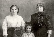 A black-and-white photo twos two adult women standing on either side of a young girl.