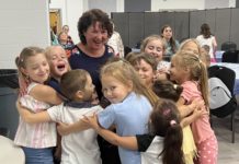 Several young children surround Victoria Faykin in a group hug.