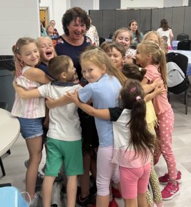 Several young children surround Victoria Faykin in a group hug.
