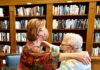 Two women embrace in a hug. They are standing in front of a book shelf.