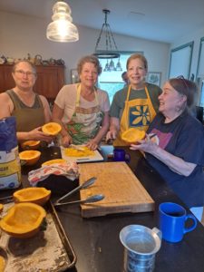 A group of women gather around a kitchen island filled with sliced pumpkin.