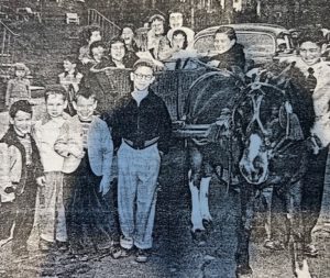 In a black-and-white photo, several children are posing outside with a horse.