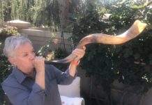 Susan Weiss is a white woman with short, grey hair holding up a long shofar.